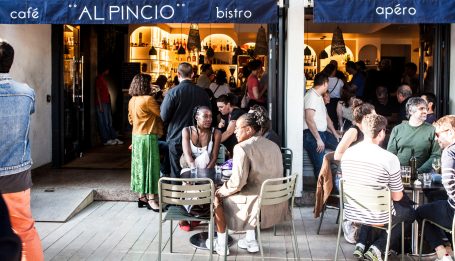 Un café animé avec des clients assis et debout à l'extérieur, ambiance conviviale.